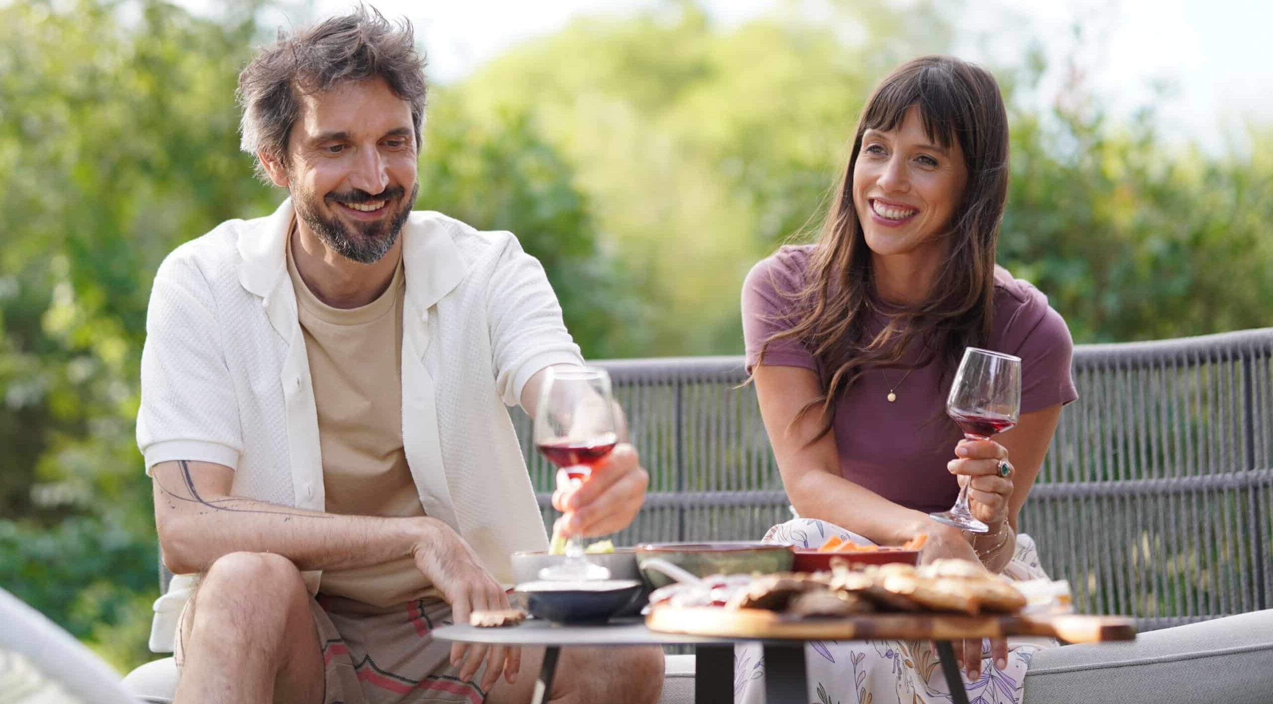 Un homme et une femme avec deux verres de vin rouge devant une table basse et des tartines