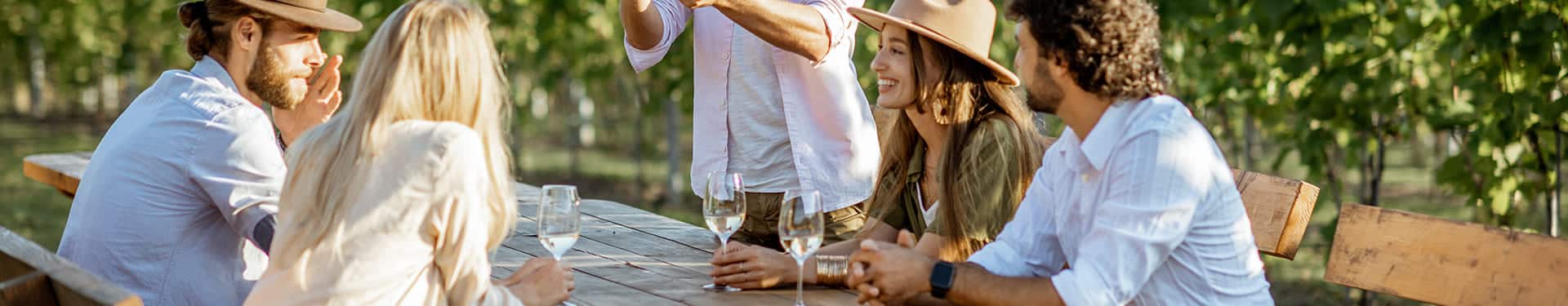 5 personnes partagent un verre de vin sur une table en bois en extérieur