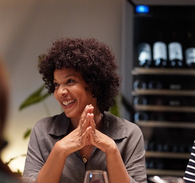 Une femme souriante assise à une table derrière une cave à vin vitrée et lumineuse