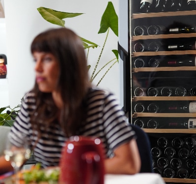 Une femme assise à une table derrière une cave à vin vitrée