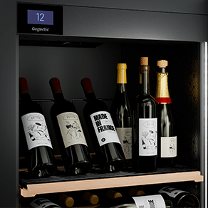 Six bouteilles de vin sont présentées verticalement sur la première étagère d'une cave à vin noire.