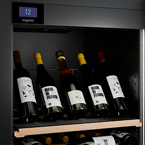 Cinq bouteilles de vin sont présentées sur le haut d'une étagère d'une cave à vin noire.