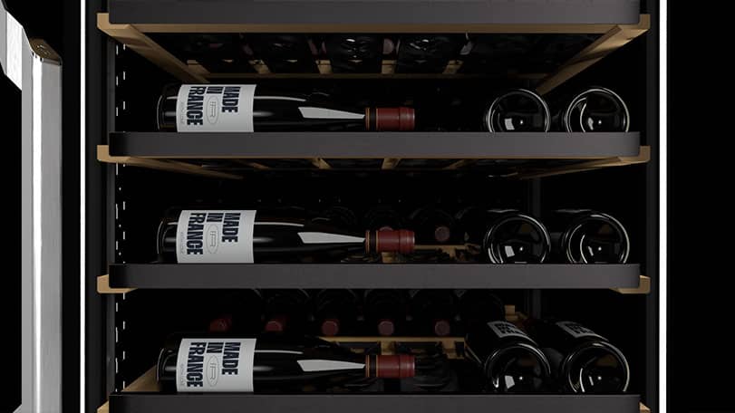Plusieurs bouteilles de vin couchées sur trois clayettes noires dans une cave à vin.