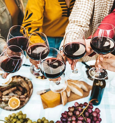 Plusieurs personnes trinquent avec des verres de vin rouge au-dessus d'une table.