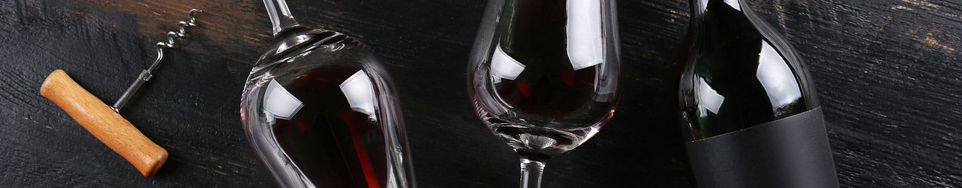 Deux verres de vin rouge, une bouteille de vin et un tire-bouchon posés sur une table en bois noire.